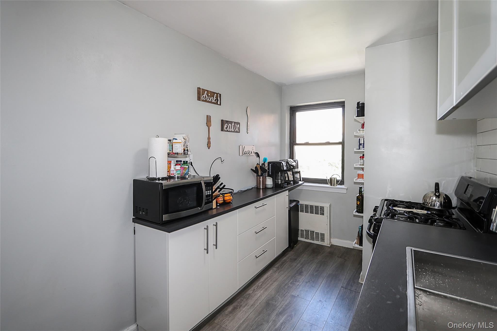 147-10 84th Road, Unit 6K Queens, NY 11435 - Photo 11 of 21 Kitchen with white cabinetry, dark countertops, dark wood-type flooring, stainless steel microwave, and radiator heating unit