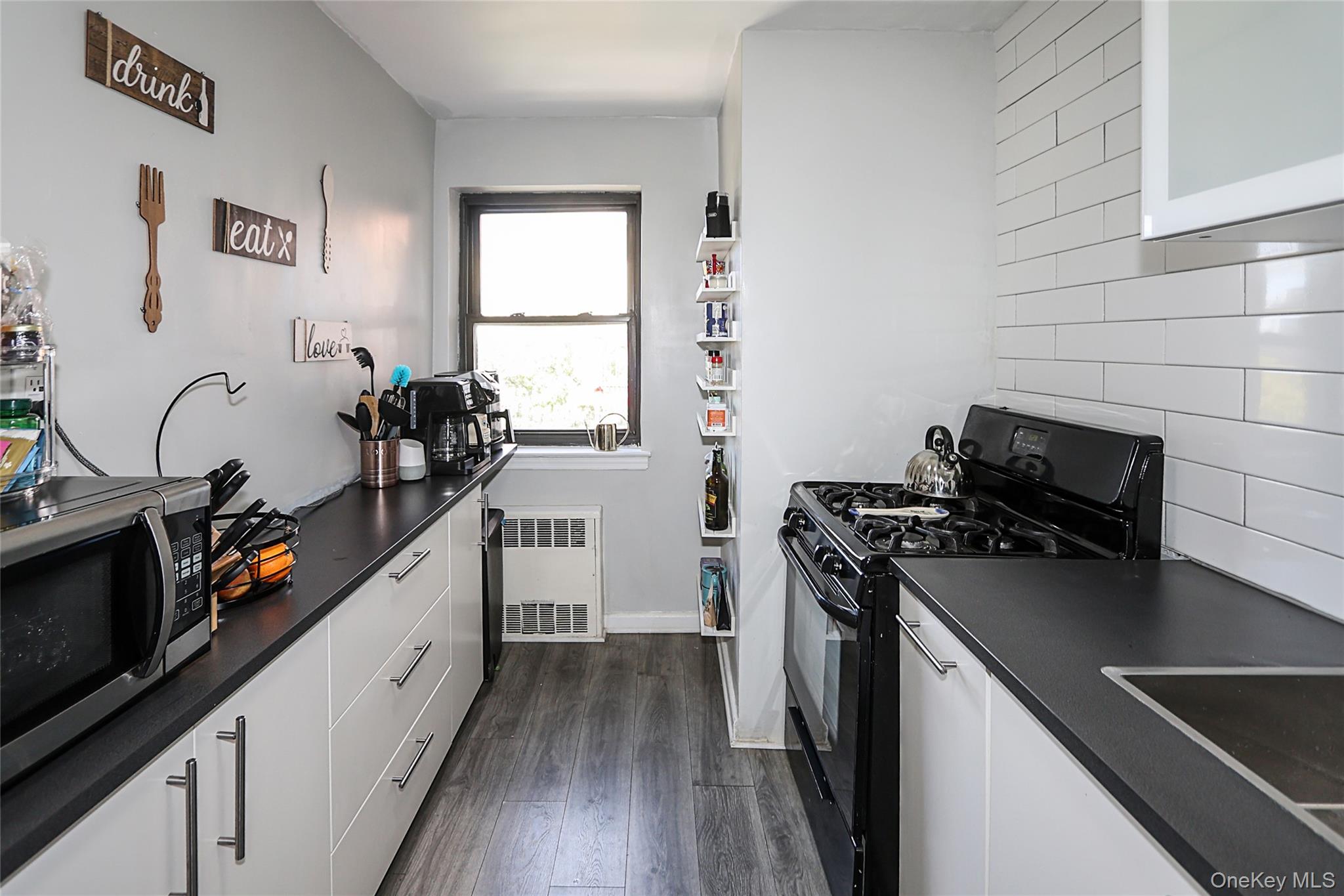 147-10 84th Road, Unit 6K Queens, NY 11435 - Photo 12 of 21 Kitchen featuring dark countertops, black range with gas cooktop, dark wood-style flooring, white cabinets, and stainless steel microwave