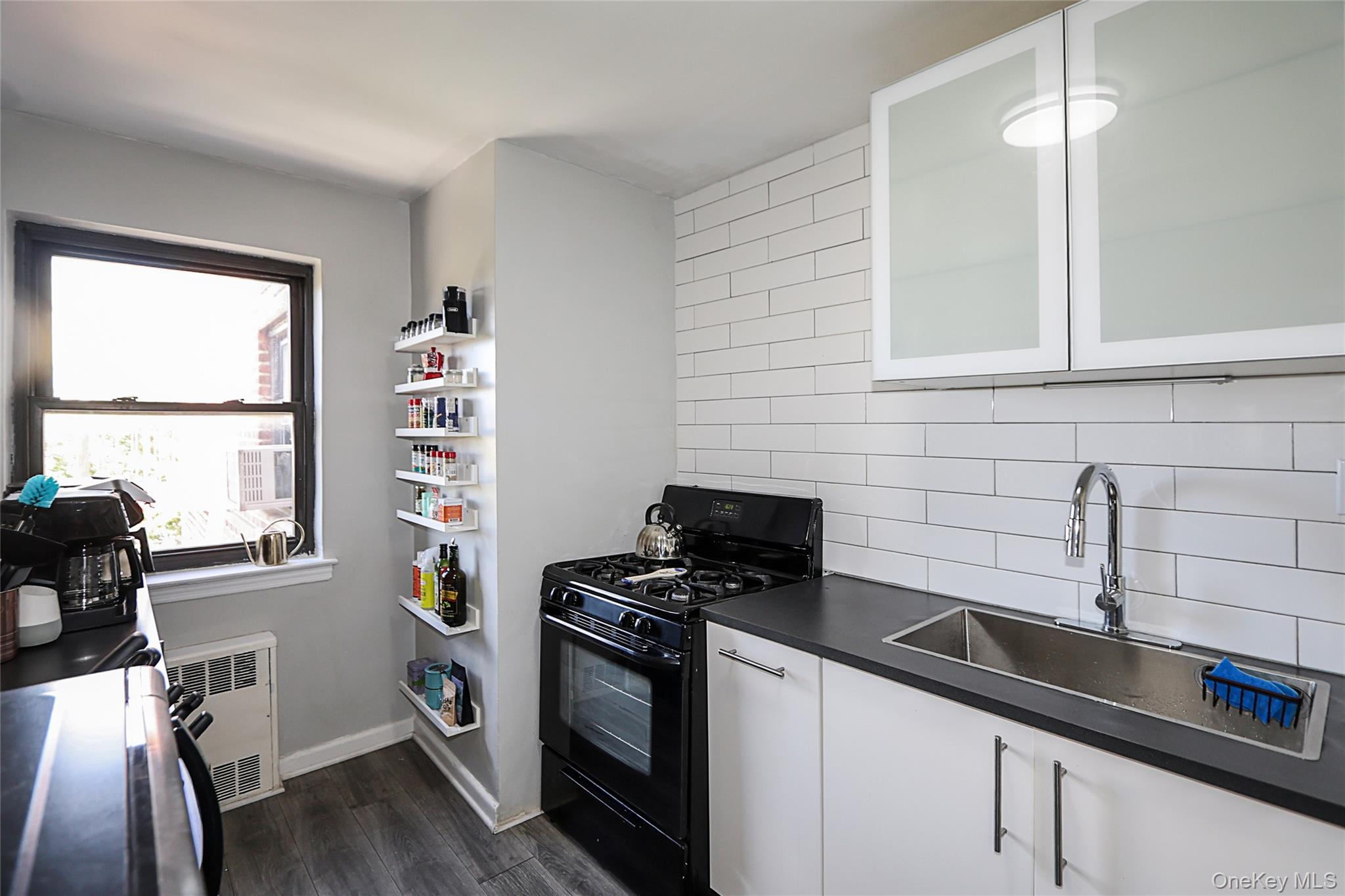 147-10 84th Road, Unit 6K Queens, NY 11435 - Photo 13 of 21 Kitchen featuring white cabinets, black gas range, dark countertops, dark wood-type flooring, and tasteful backsplash