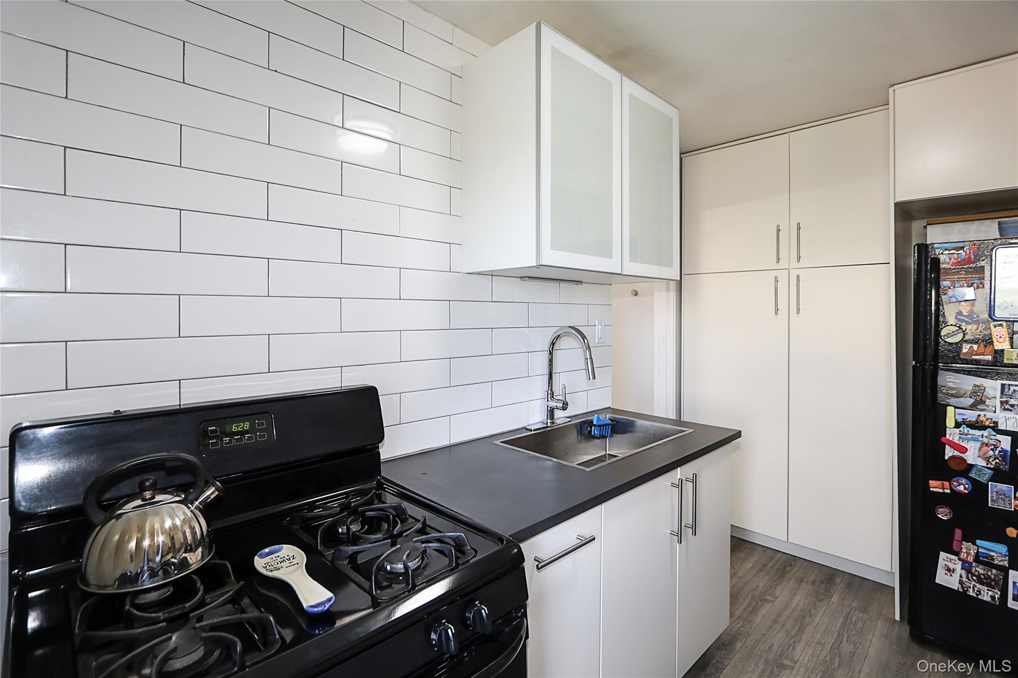 147-10 84th Road, Unit 6K Queens, NY 11435 - Photo 15 of 21 Kitchen featuring black appliances, dark countertops, white cabinets, and backsplash