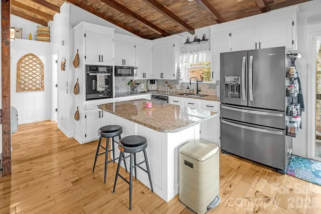 a kitchen with stainless steel appliances granite countertop a refrigerator a sink a stove and white cabinets with wooden floor