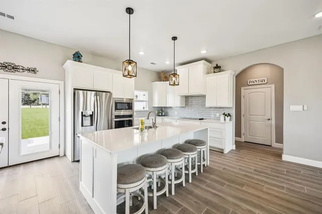 a large kitchen with kitchen island a refrigerator a stove a sink a dining table and chairs with wooden floor