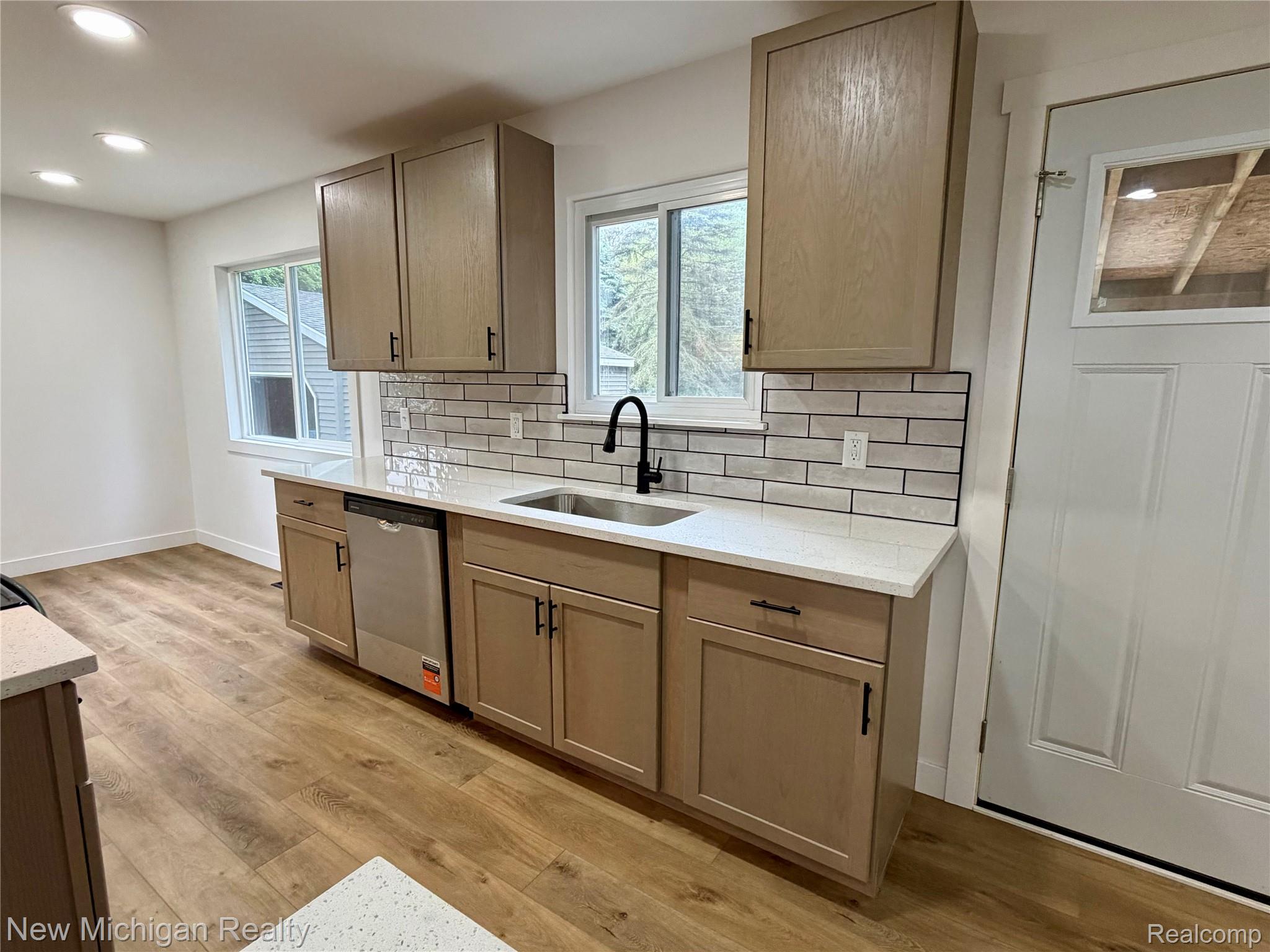 7104 Willard Road Millington, MI 48746 - Photo 10 of 30 Newly renovated kitchen featuring wood-finish flooring, light wood cabinetry with black hardware, white subway tile backsplash, and light-colored countertops