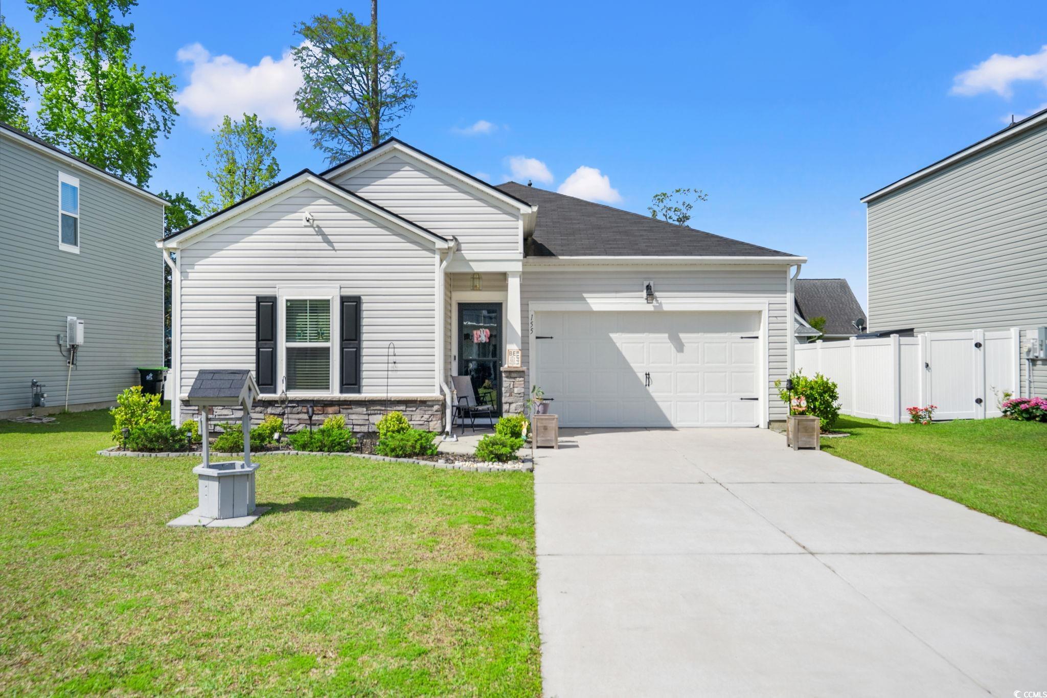 View of front of home with a front yard, stone siding, fence, a garage, and driveway