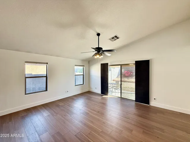 an empty room with wooden floor chandelier fan and windows