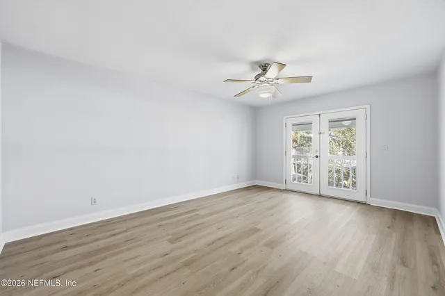 a view of an empty room with wooden floor and a ceiling fan