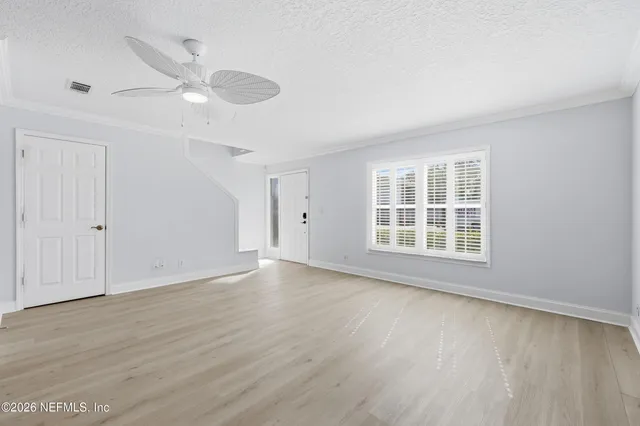 an empty room with wooden floor fan and windows