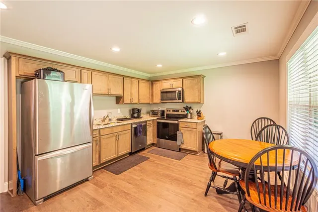 a kitchen with stainless steel appliances granite countertop a refrigerator a stove a sink a dining table and chairs with wooden floor