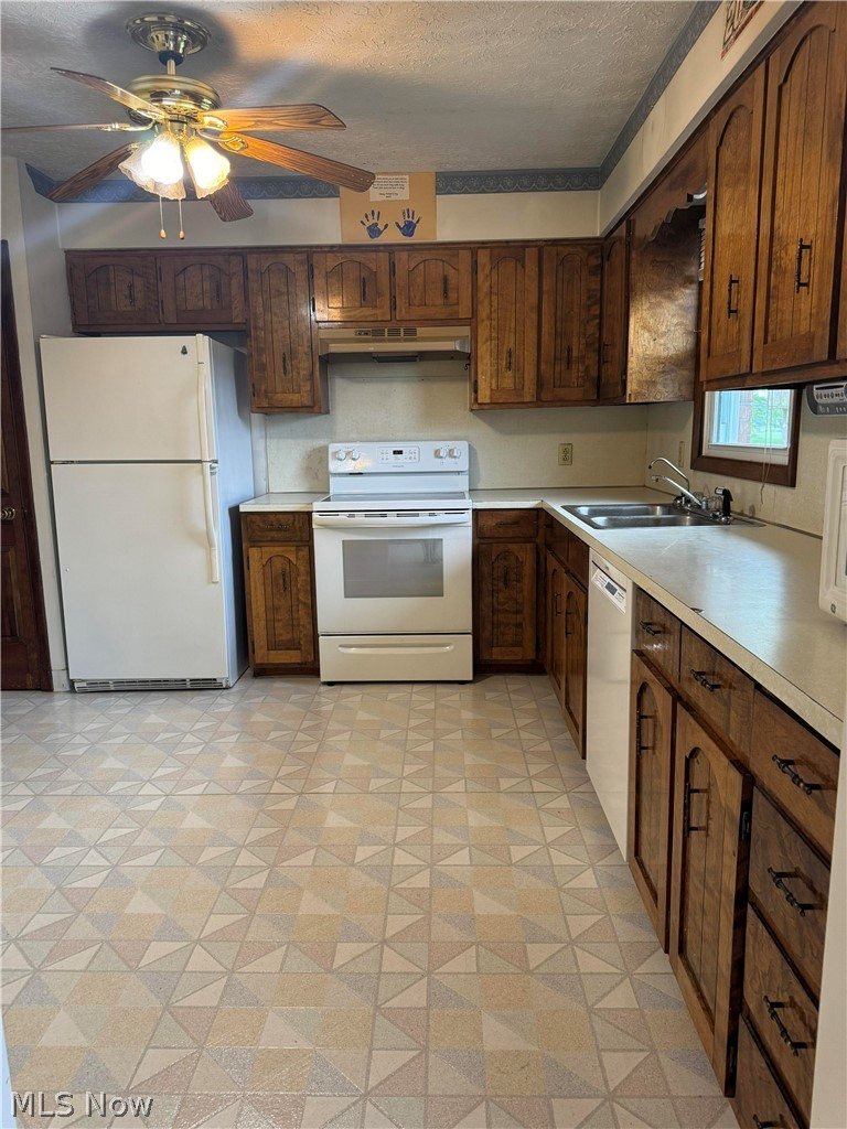 Kitchen featuring a textured ceiling, white appliances, sink, light tile flooring, and ceiling fan