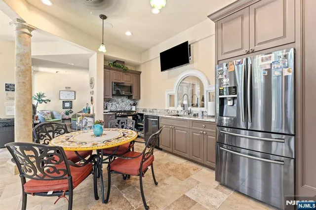 a kitchen with stainless steel appliances granite countertop a dining table chairs refrigerator and sink