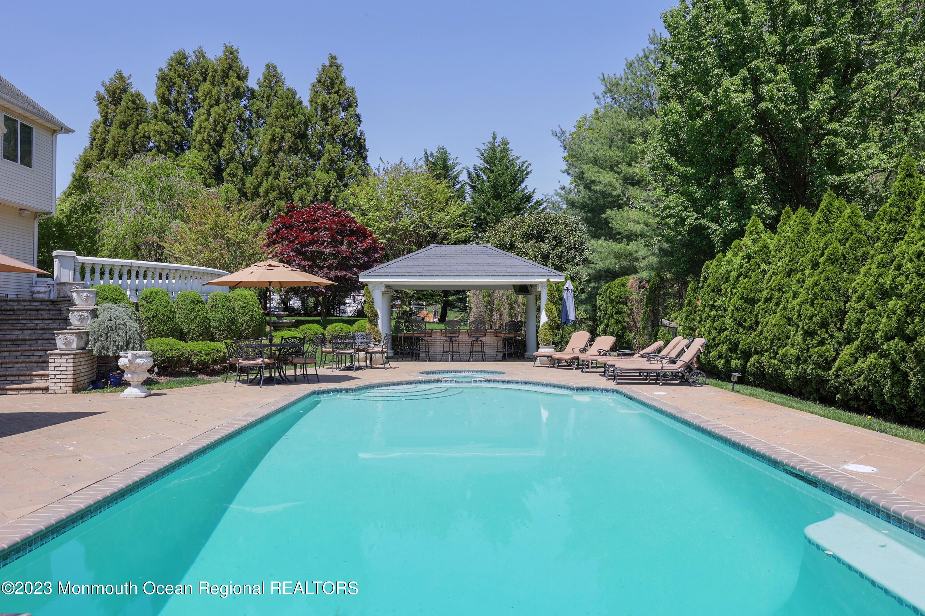 8 Old Stable Way Colts Neck, NJ 07722 - Photo 37 of 45 a view of a swimming pool with lawn chairs under an umbrella