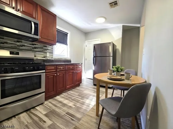 a kitchen with stainless steel appliances granite countertop a stove a refrigerator a dining table and chairs with wooden floor
