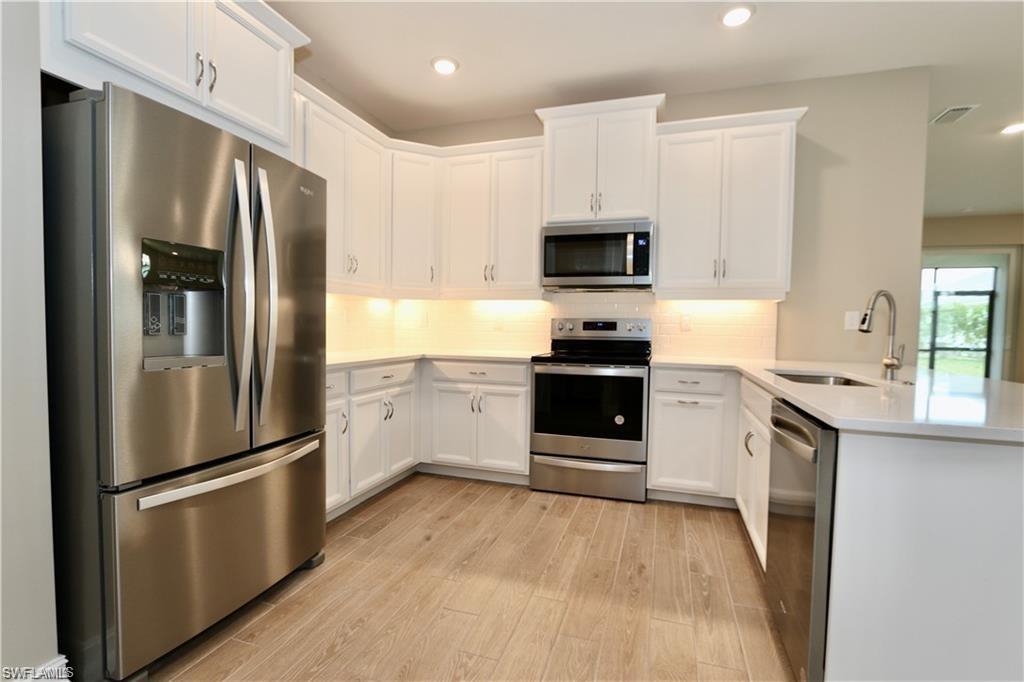 1063 Enbrook Loop Naples, FL 34114 - Photo 4 of 26 Kitchen featuring appliances with stainless steel finishes, white cabinetry, light wood-type flooring, a peninsula, and decorative backsplash