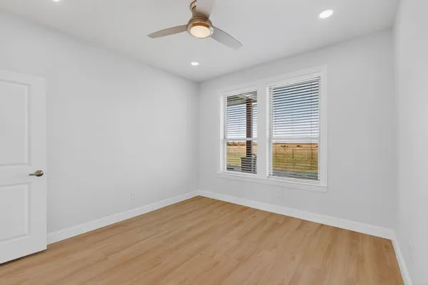 an empty room with wooden floor chandelier fan and windows