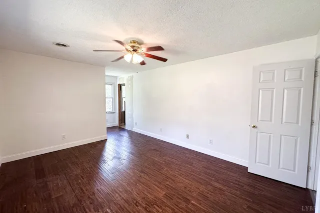 a view of an empty room with wooden floor and a ceiling fan