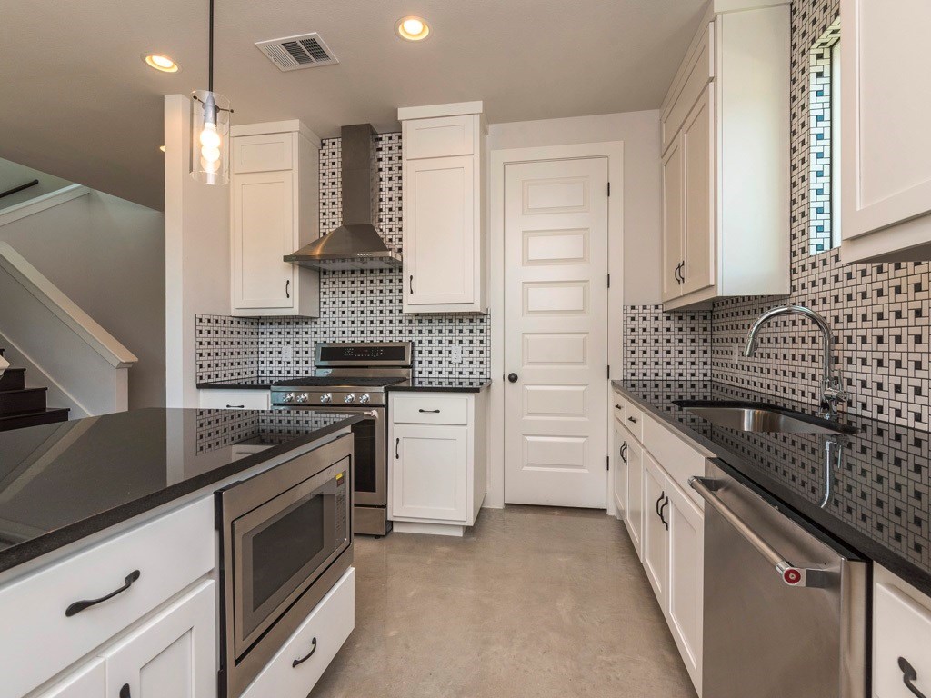 1182 Ridgeway Drive, Unit A Austin, TX 78702 - Photo 10 of 27 Kitchen with white cabinetry, dark stone counters, stainless steel appliances, finished concrete flooring, and hanging light fixtures