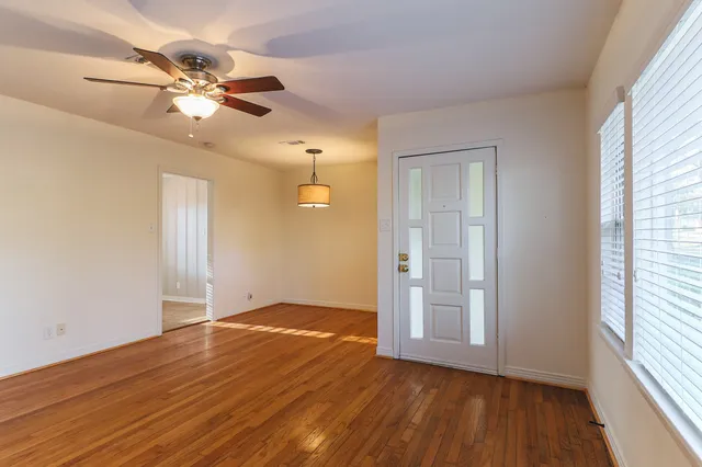 an empty room with wooden floor fan and windows
