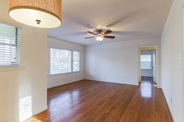 an empty room with wooden floor chandelier fan and windows