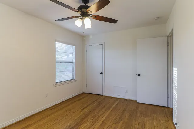 an empty room with wooden floor fan and windows