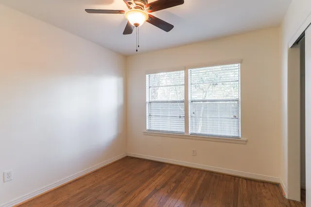 an empty room with wooden floor fan and windows