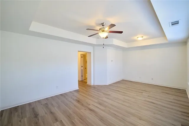 an empty room with wooden floor chandelier fan and windows