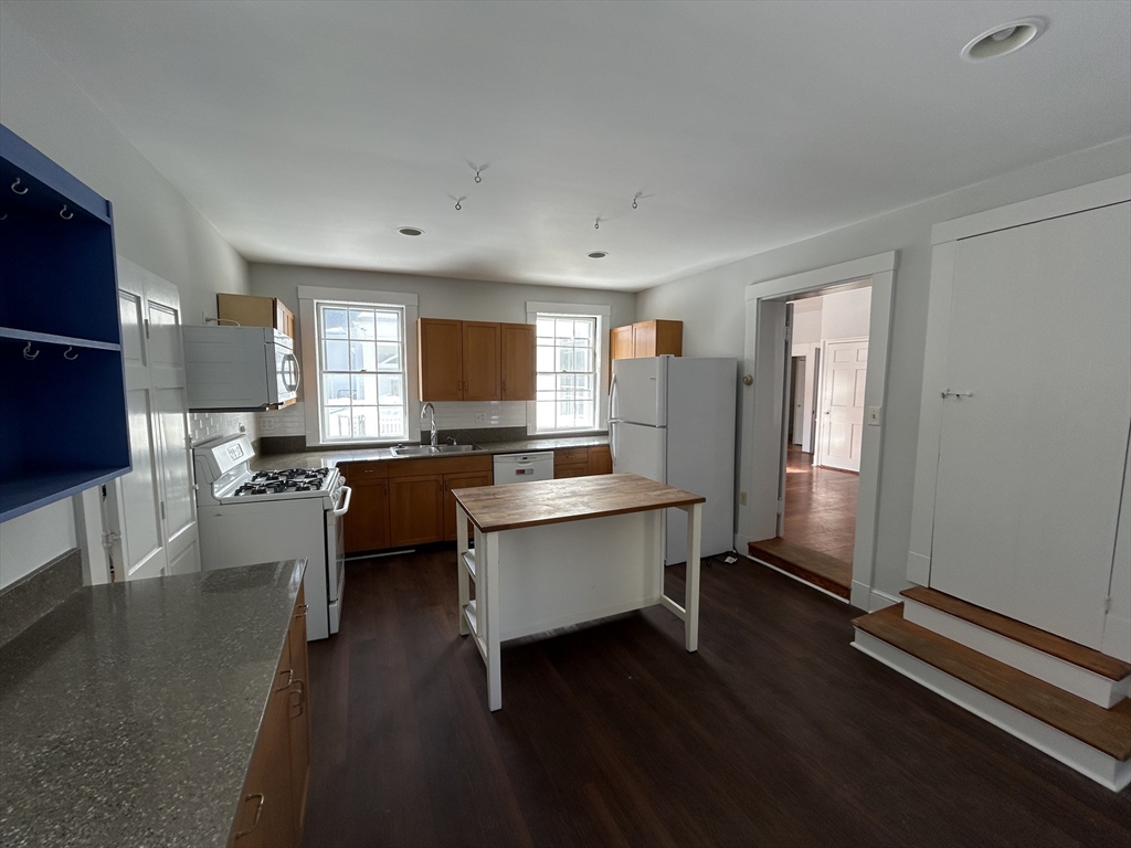 660 High Street Dedham, MA 02026 - Photo 10 of 25 a large white kitchen with a refrigerator a sink dishwasher a stove and a dining table with wooden floor