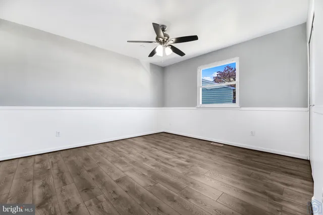 an empty room with wooden floor chandelier fan and windows