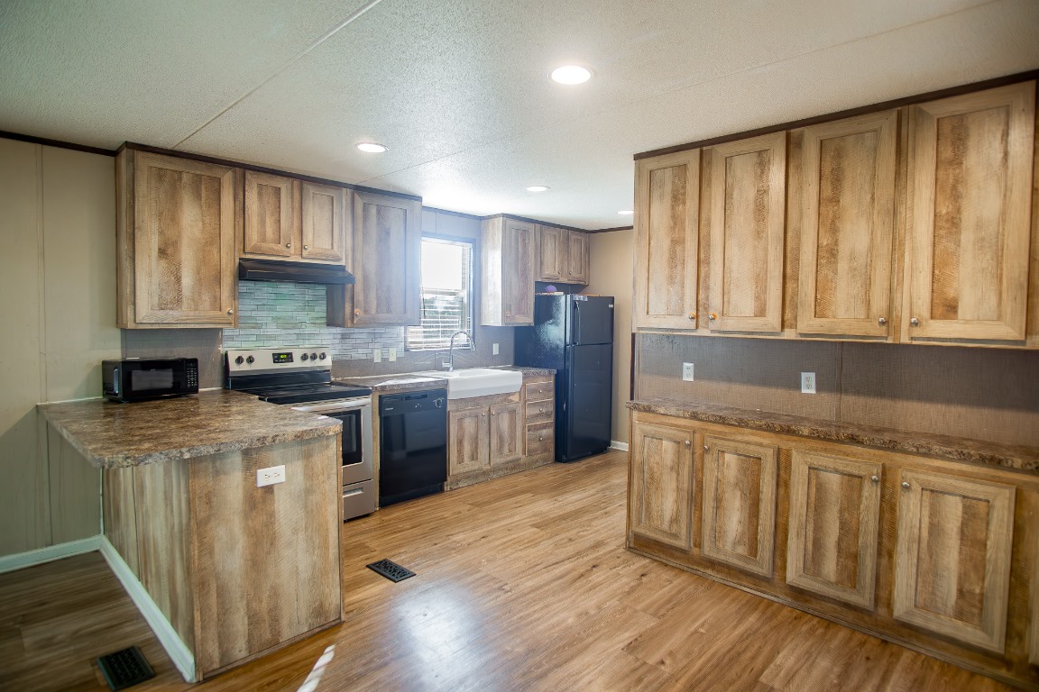 205 Arrowhead Cove Kyle, TX 78640 - Photo 4 of 20 a kitchen with granite countertop wooden floors white cabinets and stainless steel appliances