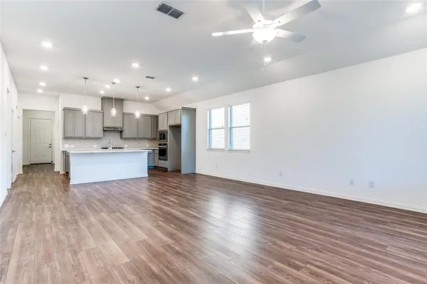a view of an empty room and kitchen with wooden floor