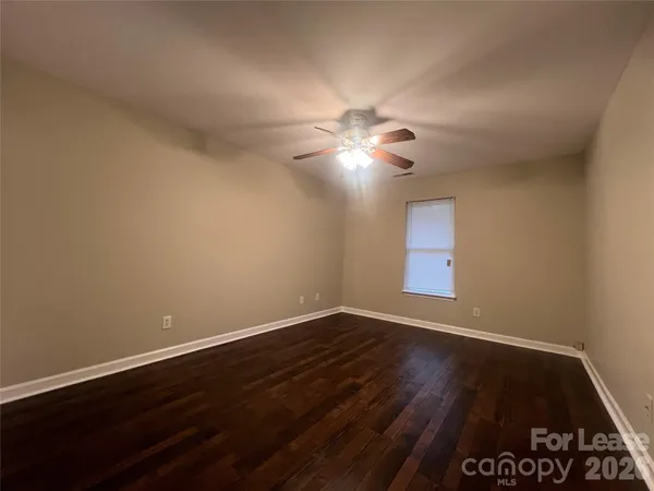 a view of an empty room with wooden floor and a fan