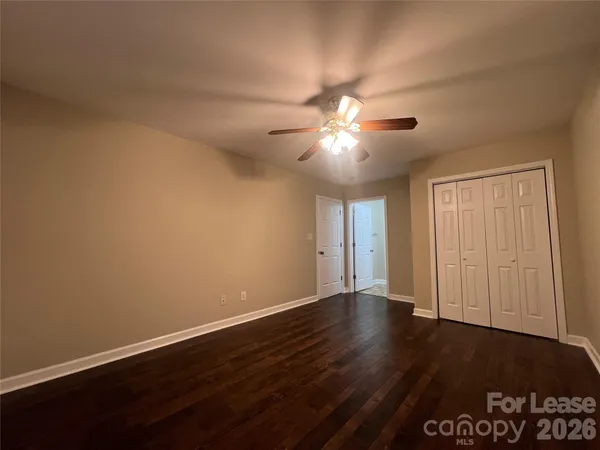 a view of an empty room with wooden floor and a chandelier fan