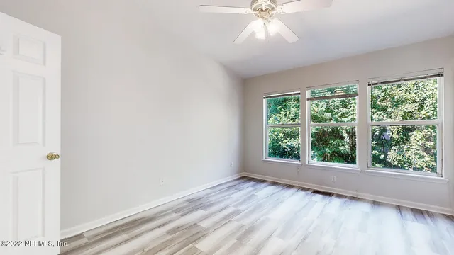 an empty room with wooden floor fan and windows