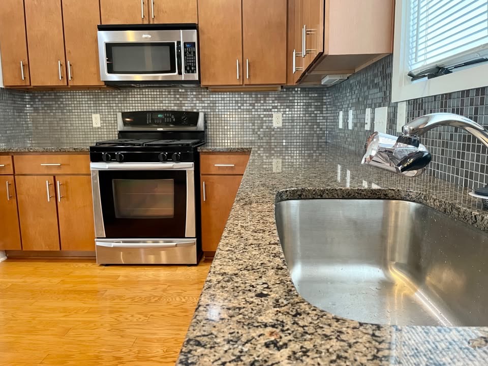 1702 South Lamar Boulevard, Unit 2 Austin, TX 78704 - Photo 2 of 25 Kitchen featuring appliances with stainless steel finishes, dark stone countertops, light wood-style floors, tasteful backsplash, and brown cabinetry