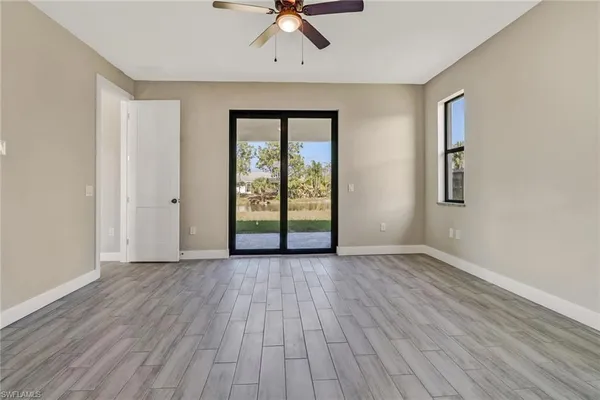 an empty room with wooden floor chandelier fan and windows