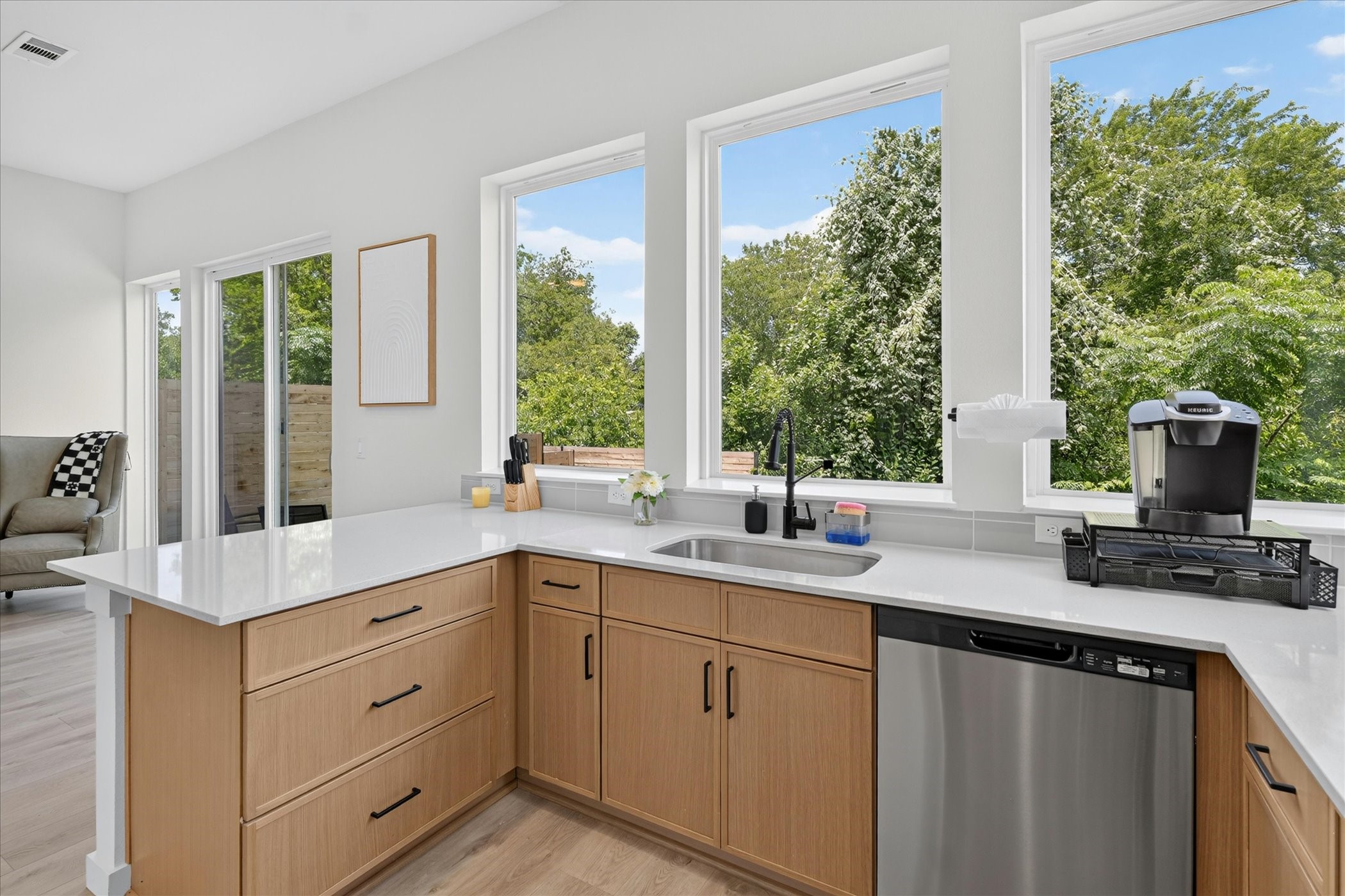 2000 Riverside Farms Road, Unit 8101 Austin, TX 78741 - Photo 6 of 41 This modern kitchen features sleek white countertops, light wood cabinetry, and stainless steel appliances. Large windows provide abundant natural light and a scenic view of lush greenery, creating a bright and inviting space.