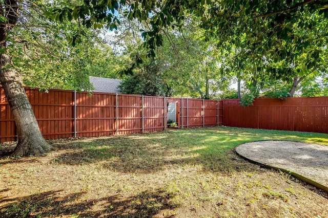 a backyard of a house with large trees and wooden fence