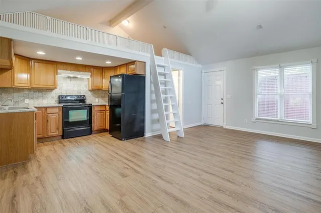 an empty room with wooden floor kitchen view and windows