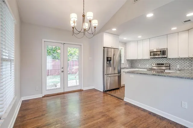 a view of a kitchen with stainless steel appliances granite countertop a refrigerator a stove a sink dishwasher and white cabinets with wooden floor