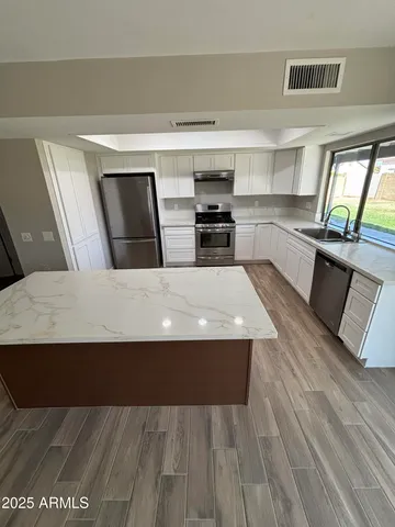 a living room with stainless steel appliances furniture a kitchen island wooden floor and a window