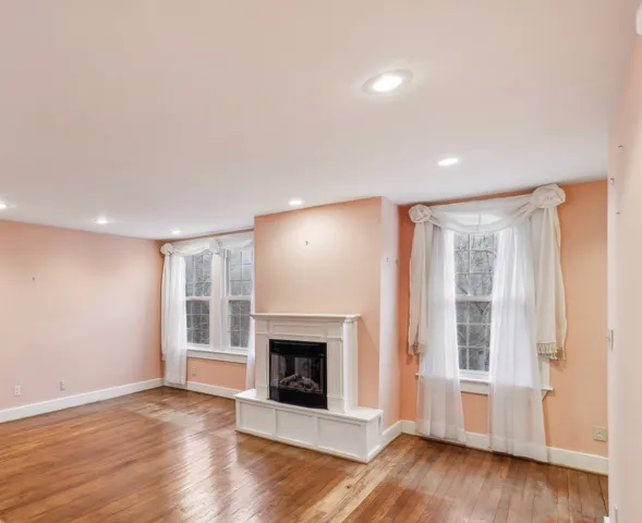 a view of an empty room with wooden floor fireplace and a window