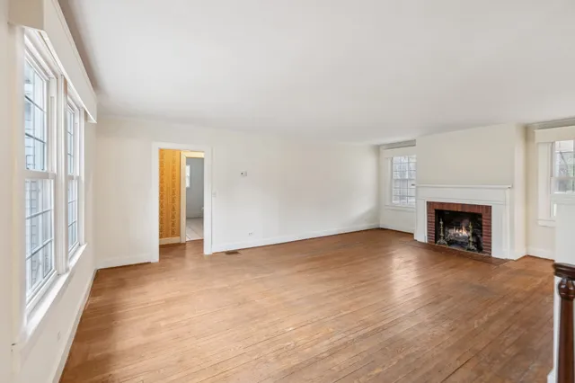 a view of an empty room with wooden floor fireplace and a window