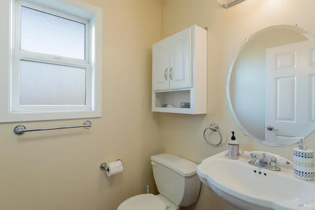 a bathroom with a granite countertop toilet a sink a mirror and a window