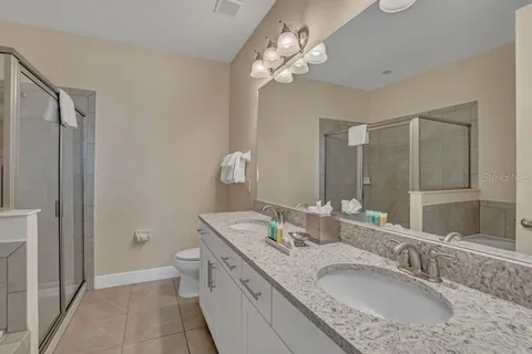a bathroom with a granite countertop double vanity sink a mirror and a shower