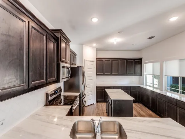 a kitchen with stainless steel appliances kitchen island granite countertop a refrigerator and a stove top oven with wooden floor