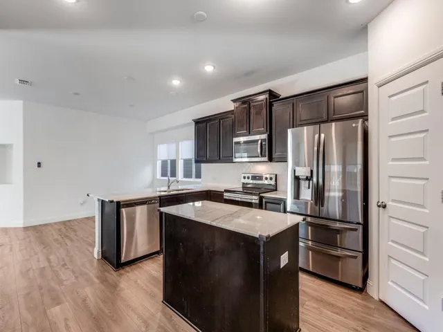 a kitchen with stainless steel appliances a sink a stove a refrigerator cabinets and wooden floor