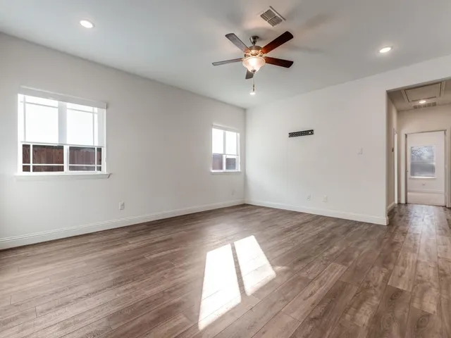 an empty room with wooden floor chandelier fan and windows