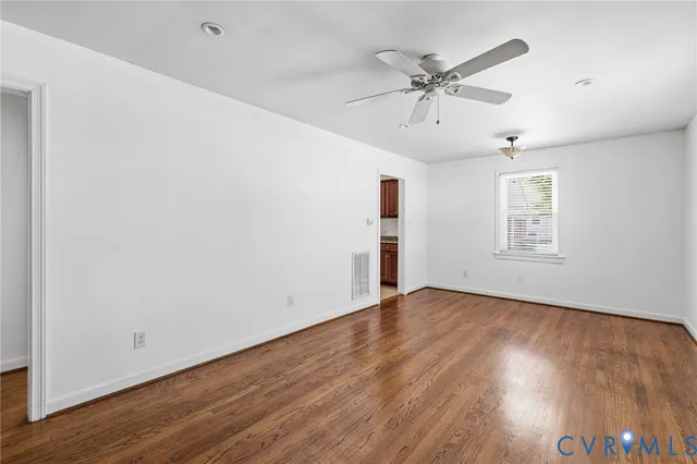 an empty room with wooden floor ceiling fan and windows