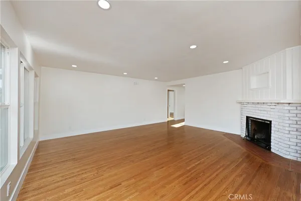 an empty room with wooden floor fireplace and windows