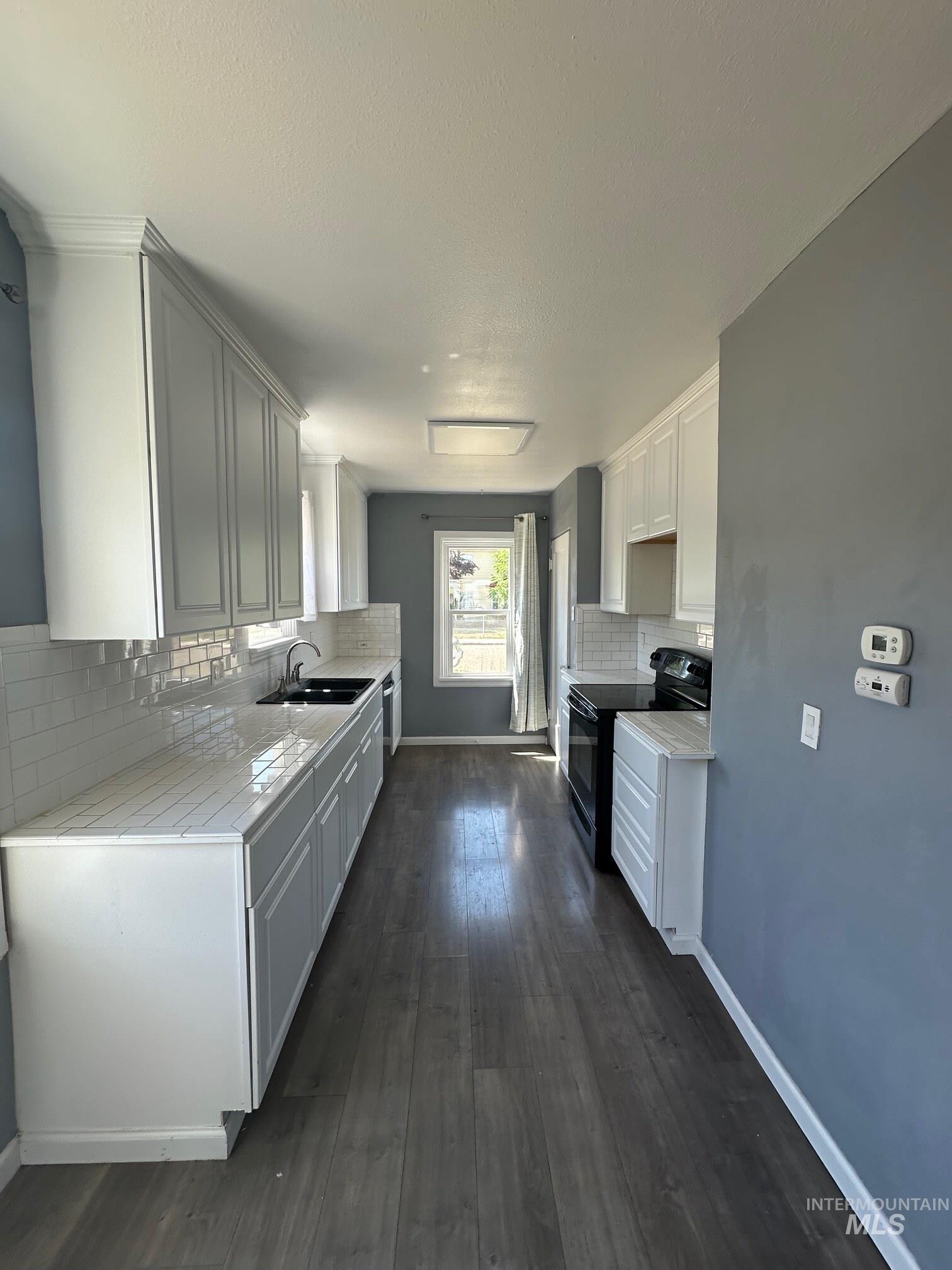 787 Southwest 3rd Street Ontario, OR 97914 - Photo 2 of 22 Kitchen with black range with electric stovetop, decorative backsplash, dark wood-style floors, and a textured ceiling