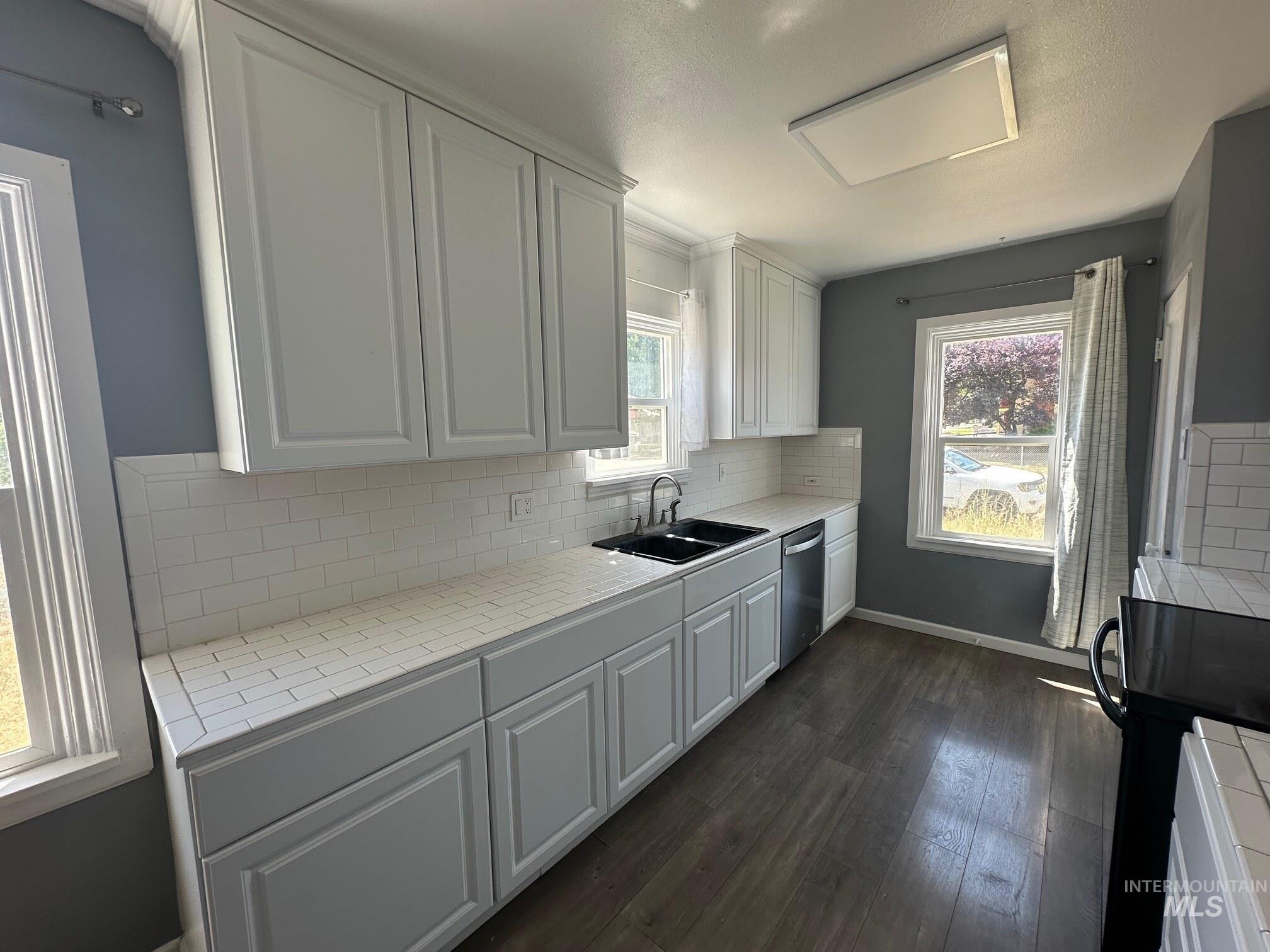 787 Southwest 3rd Street Ontario, OR 97914 - Photo 3 of 22 Kitchen featuring backsplash, dark wood-style floors, white cabinetry, and light countertops